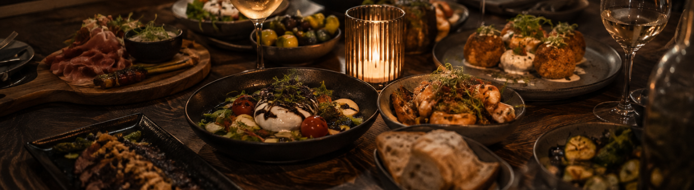 Restaurant – Sharing-Tisch Verschiedene kleine Gerichte zum Teilen auf einem Tisch bei Kerzenlicht
